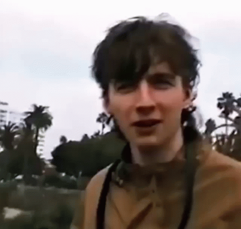 A Young Man Wearing Headphones And A Camera Is Standing In Front Of Palm Trees . GIF