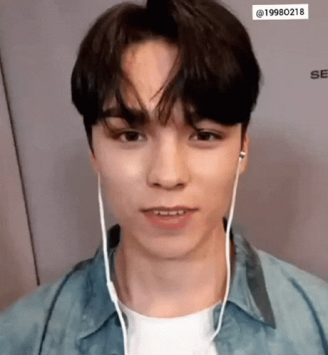 A Young Man Wearing Headphones And A Denim Shirt Looks At The Camera . GIF