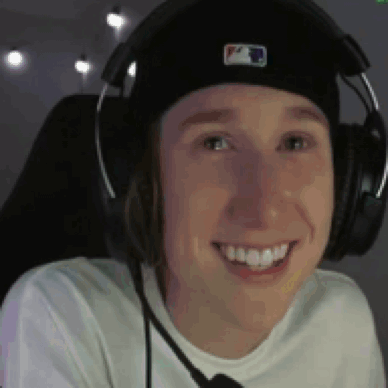 a young man wearing headphones and a hat is smiling while sitting in a chair .