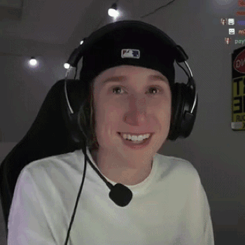 a young man wearing headphones and a hat is smiling while sitting in a chair .