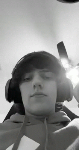 A Young Man Wearing Headphones And A Hoodie Is Taking A Selfie . GIF