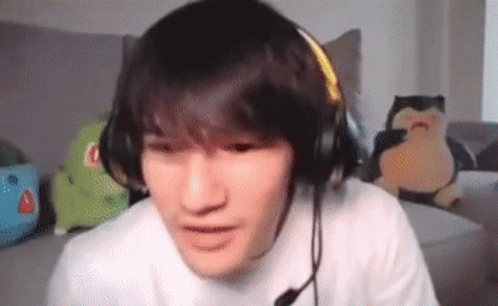 A Young Man Wearing Headphones And A Microphone Is Sitting On A Couch In A Living Room . GIF