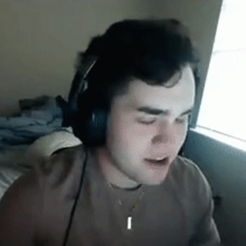 A Young Man Wearing Headphones And A Necklace Is Sitting In Front Of A Window . GIF