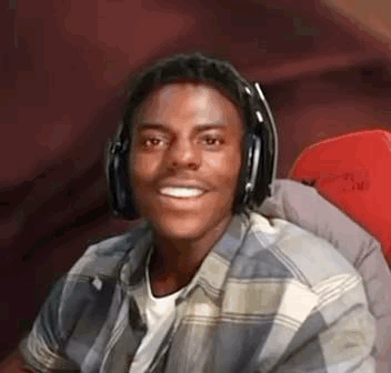 A Young Man Wearing Headphones And A Plaid Shirt Is Smiling While Sitting In A Chair . GIF