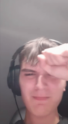A Young Man Wearing Headphones Is Covering His Face With His Hand GIF