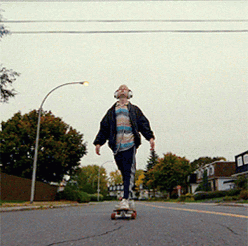 a young man wearing headphones is riding a skateboard down a street