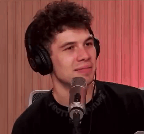 A Young Man Wearing Headphones Is Sitting In Front Of A Microphone And Smiling . GIF