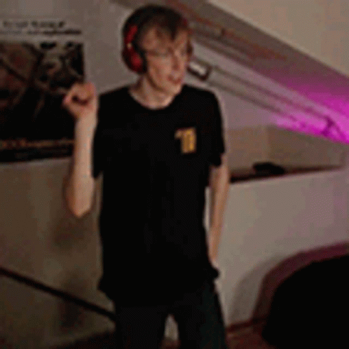 A Young Man Wearing Headphones Is Standing In A Room . GIF