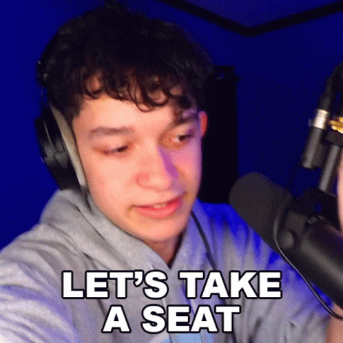 A Young Man Wearing Headphones Is Talking Into A Microphone And Says Let 'S Take A Seat GIF