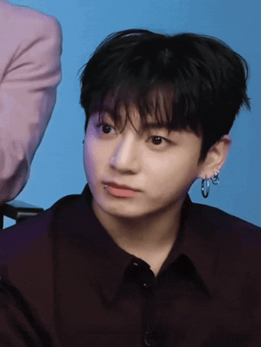 a young man wearing hoop earrings and a black shirt looks at the camera