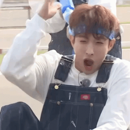 A Young Man Wearing Overalls And A Headband Is Yawning While Sitting Down . GIF