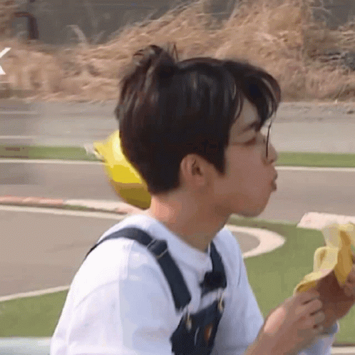 A Young Man Wearing Overalls Is Eating A Banana GIF