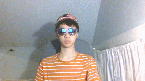 A Young Man Wearing Sunglasses And A Baseball Cap Looks At The Camera GIF