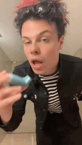 A Young Man Wearing Sunglasses And A Striped Shirt Is Holding A Blue Inhaler In His Hand GIF