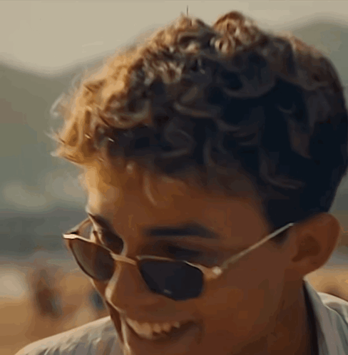 A Young Man Wearing Sunglasses Is Smiling And Looking At The Camera GIF