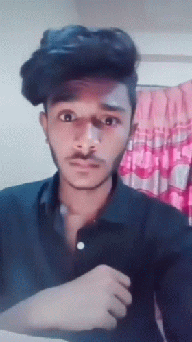 A Young Man With A Mustache Is Making A Funny Face While Wearing A Black Shirt . GIF