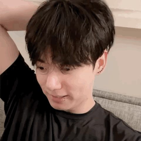 a young man with a piercing in his lip is sitting on a couch with his hand on his head .