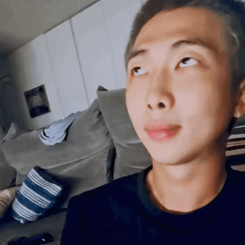 A Young Man With A Shaved Head Is Sitting On A Couch Looking Up At Something . GIF