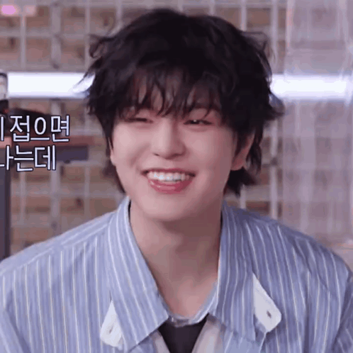 A Young Man With A Striped Shirt And Tie Is Smiling And Looking At The Camera . GIF