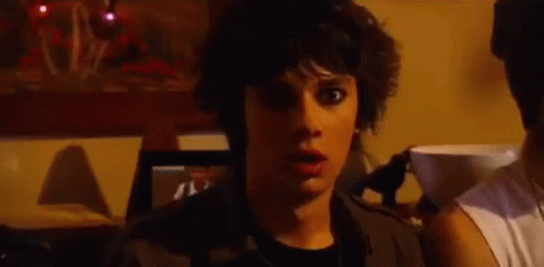 A Young Man With A Surprised Look On His Face Is Standing In A Dark Room . GIF