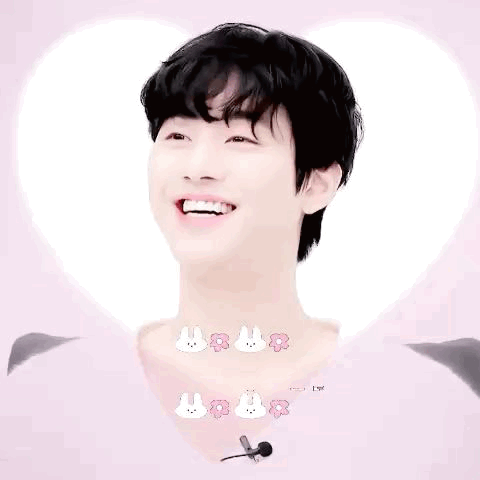A Young Man With Black Hair Is Smiling In Front Of A Heart . GIF