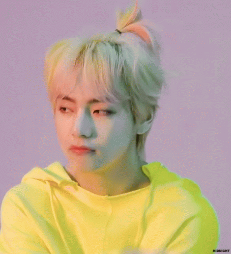 A Young Man With Blonde Hair In A Ponytail Is Wearing A Bright Yellow Hoodie . GIF