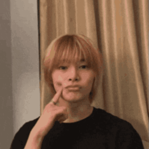 A Young Man With Blonde Hair Is Making A Funny Face While Holding His Finger To His Face . GIF