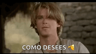 A Young Man With Blonde Hair Is Sitting In Front Of A Brick Wall And Saying `` Como Desees '' . GIF