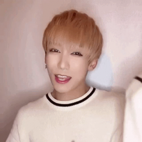 A Young Man With Blonde Hair Is Wearing A White Sweater With A Black Stripe Around The Neck . GIF