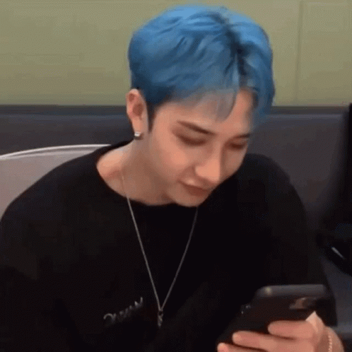 A Young Man With Blue Hair Is Looking At His Phone . GIF
