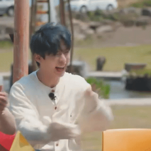 A Young Man With Blue Hair Is Sitting At A Table With His Arms Outstretched And Laughing . GIF