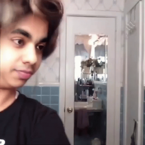 a young man with curlers in his hair is standing in front of a mirror in a bathroom .
