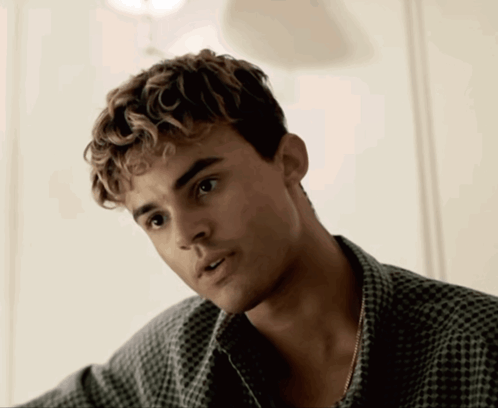 A Young Man With Curly Hair And A Plaid Shirt Looks At The Camera GIF