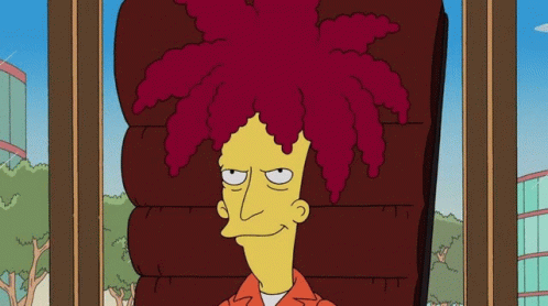 A Young Man With Curly Hair And Braces On His Teeth Looks At The Camera GIF