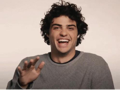 A Young Man With Curly Hair Is Laughing And Waving His Hand GIF