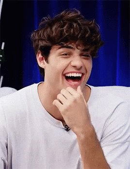 A Young Man With Curly Hair Is Laughing With His Hand On His Face . GIF