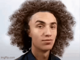 A Young Man With Curly Hair Is Looking At The Camera And Making A Funny Face . GIF