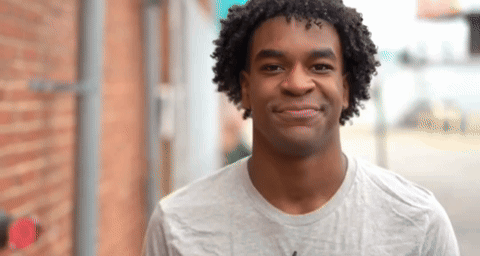 A Young Man With Curly Hair Is Smiling For The Camera GIF