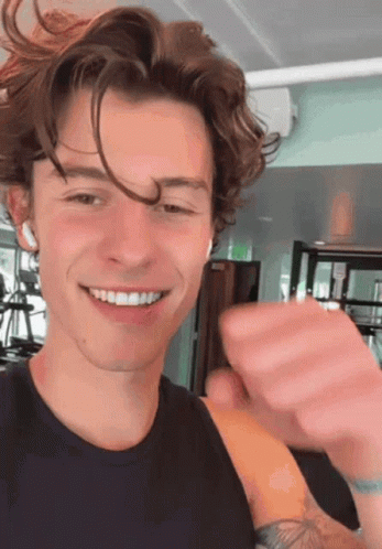 A Young Man With Curly Hair Is Smiling In A Gym While Wearing Headphones . GIF