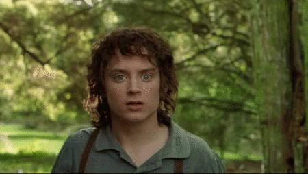 A Young Man With Curly Hair Is Standing In A Forest Looking At The Camera GIF