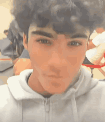 A Young Man With Curly Hair Is Taking A Selfie In A Classroom . GIF