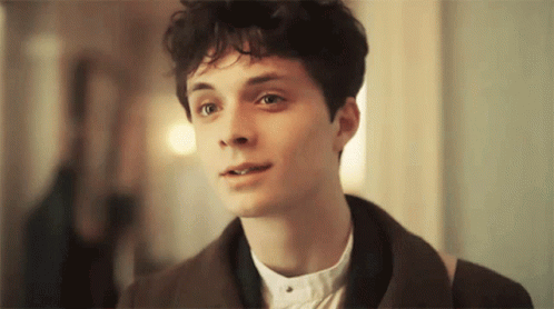 A Young Man With Curly Hair Is Wearing A Brown Jacket And A White Shirt GIF