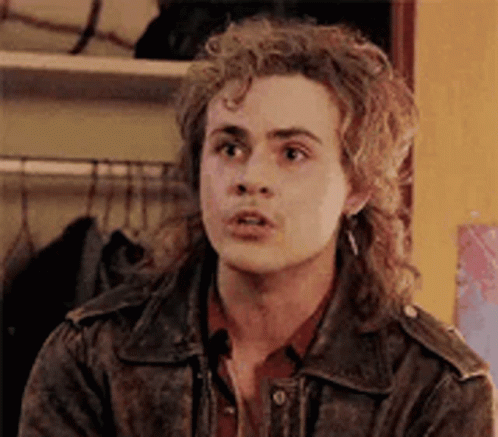 A Young Man With Curly Hair Is Wearing A Leather Jacket And Earrings . GIF