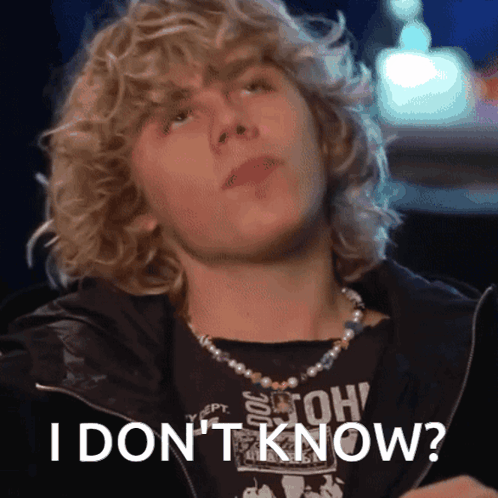 A Young Man With Curly Hair Is Wearing A Pearl Necklace And A Black Shirt That Says " I Don 'T Know " GIF