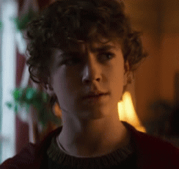 A Young Man With Curly Hair Is Wearing A Red Sweater . GIF