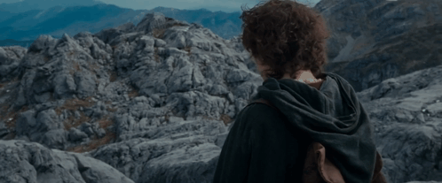 A Young Man With Curly Hair Stands In Front Of A Mountain GIF