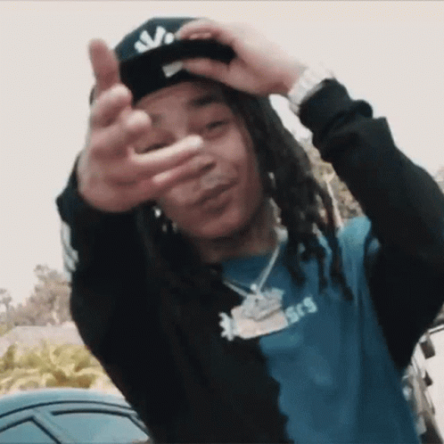 A Young Man With Dreadlocks Is Wearing A Hat And Making A Peace Sign GIF