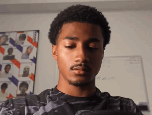 A Young Man With His Eyes Closed Is Standing In Front Of A White Board With A Picture Of A Man On It GIF
