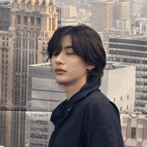 a young man with his eyes closed stands in front of a cityscape