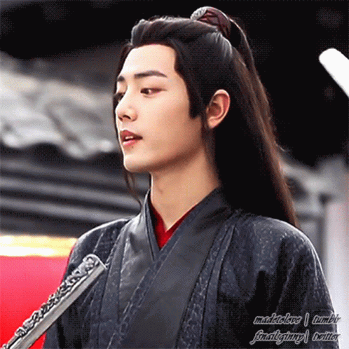 A Young Man With Long Black Hair Is Holding A Flute In His Hand . GIF
